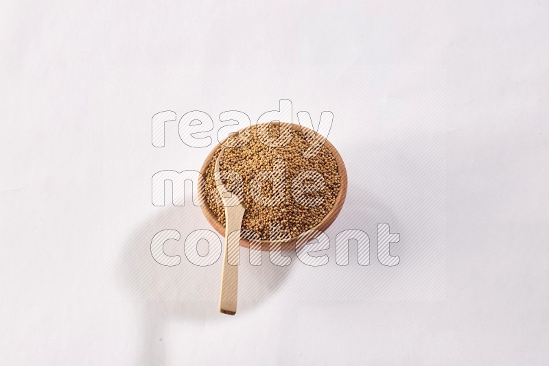A wooden bowl full of mustard seeds with a wooden spoon on the seed on a white flooring