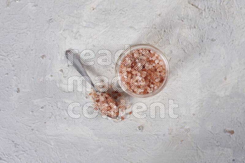 A glass jar full of coarse himalayan salt crystals on white background