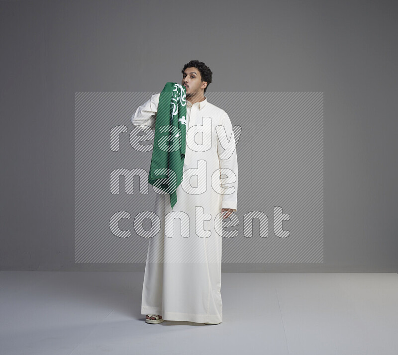 رجل سعودي يرتدي ثوب ويقبل العلم السعودي