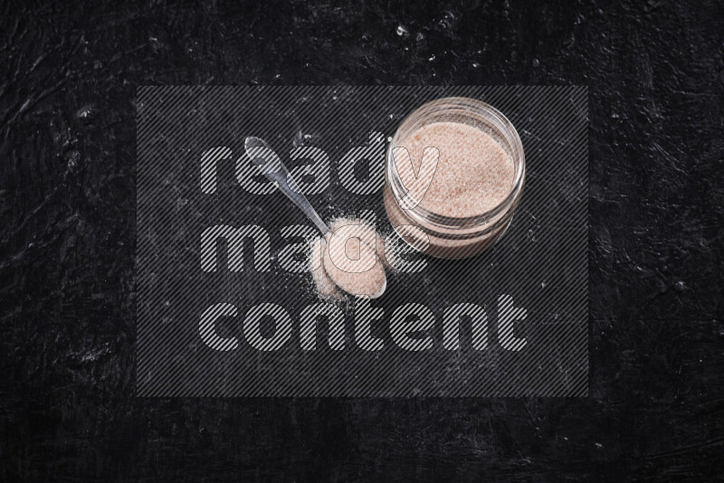 A glass jar full of fine himalayan salt on black background