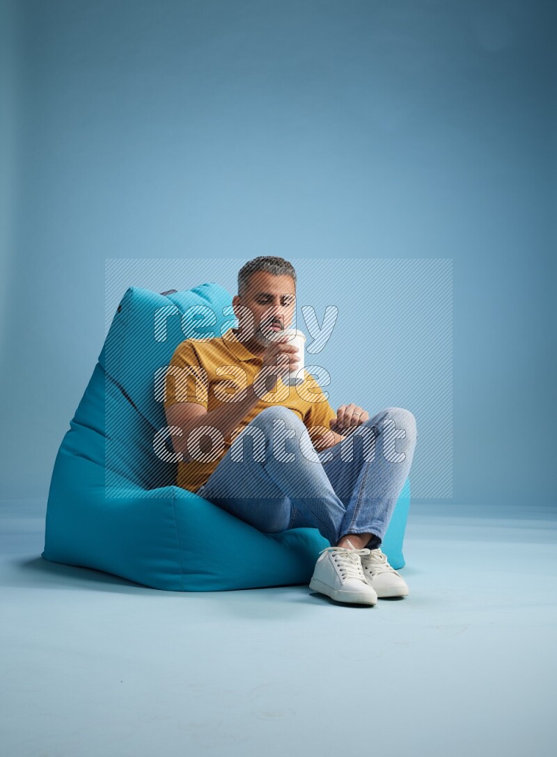 A man sitting on a blue beanbag and drinking coffee