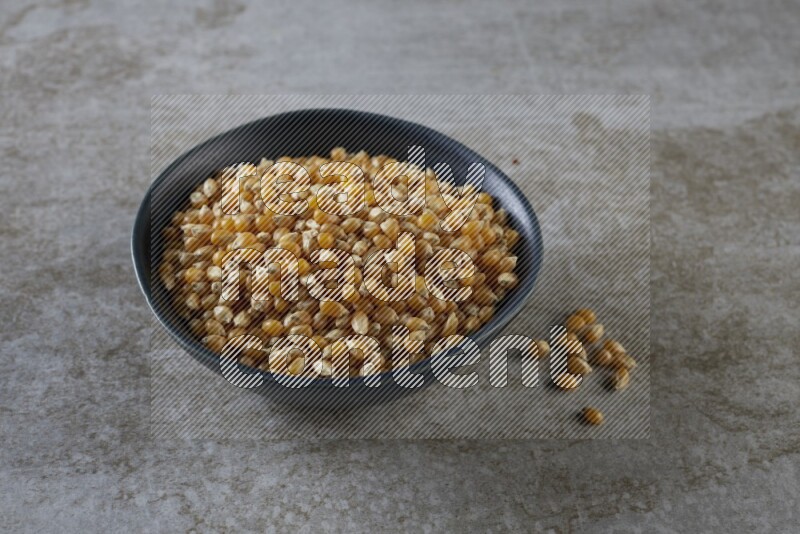 corn kernel in a black ceramic bowl on a grey textured countertop
