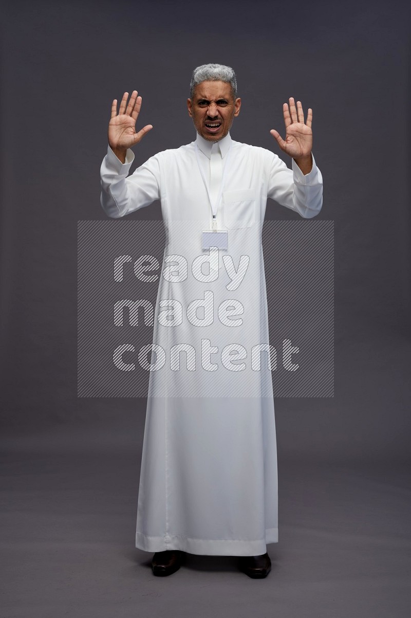 Saudi man wearing thob with neck strap employee badge standing interacting with the camera on gray background