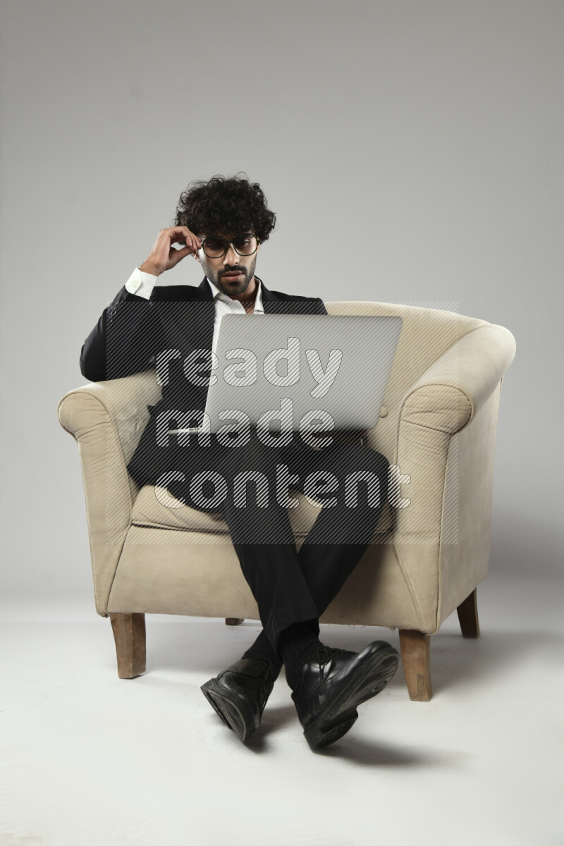 رجل يرتدي ملابس رسمية يجلس علي كرسي و يعمل علي لاب توب علي خلفية بيضاء