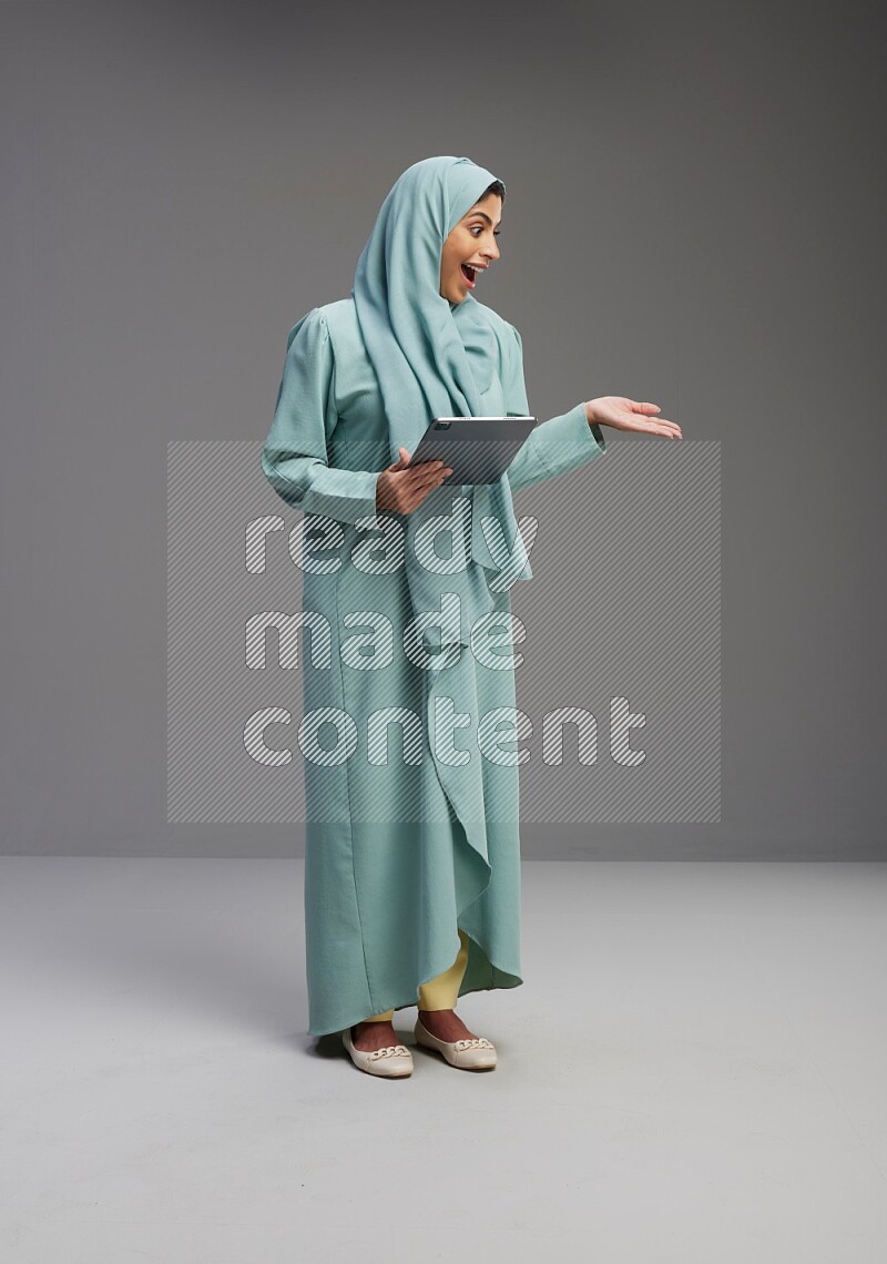 Saudi Woman wearing Abaya standing working on tablet on Gray background