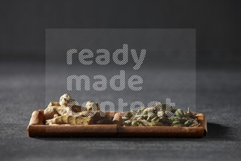 مربعان من أعواد القرفة ممتلئان بحبوب الهيل وأصابع الكركم علي خلفية سوداء