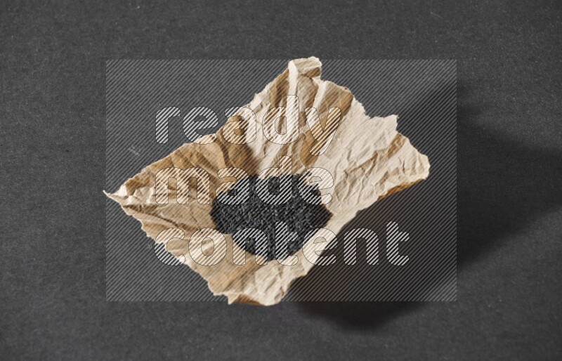 A crumpled piece of paper full of black seeds on a black flooring