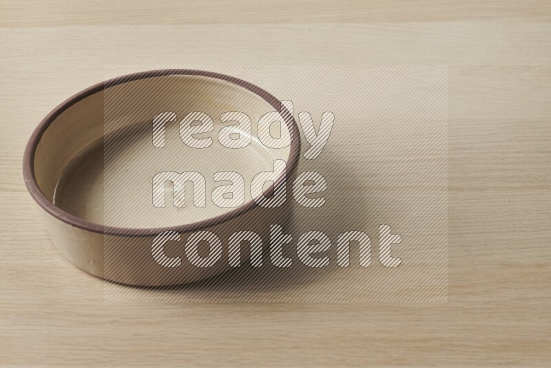 A beige pottery oven bowl on light wooden background
