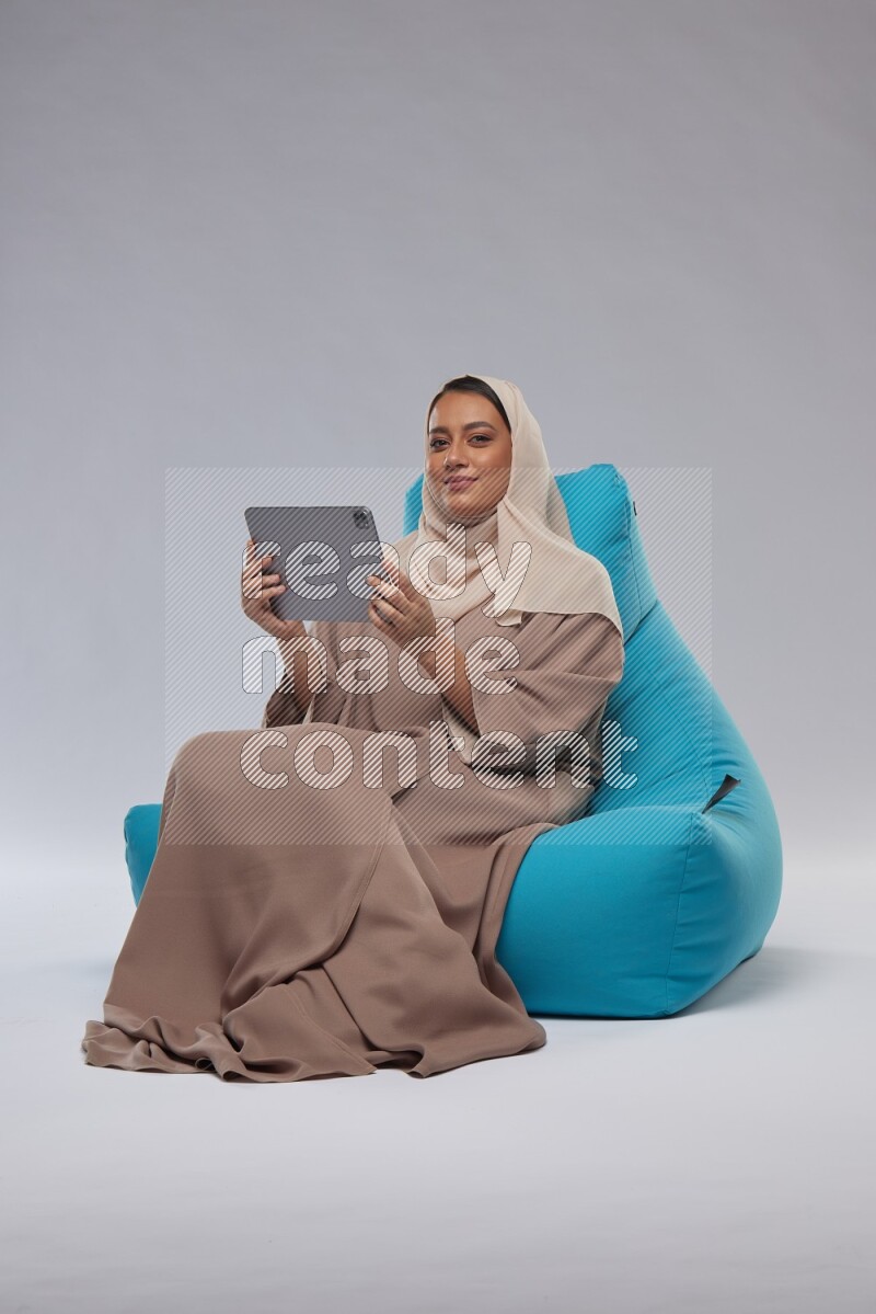A Saudi woman sitting on a blue beanbag and working on tablet