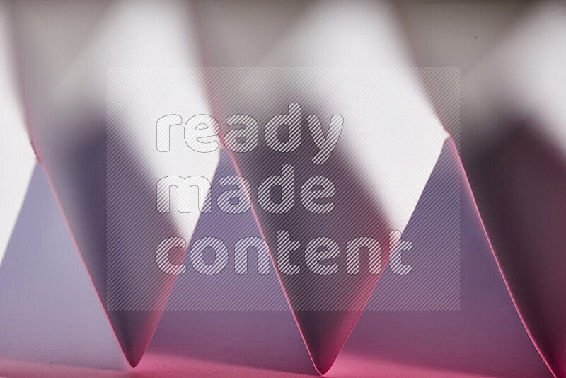 A close-up abstract image showing sharp geometric paper folds in white and pink gradients