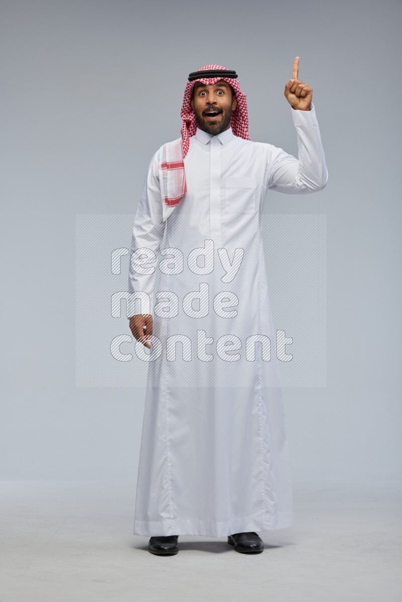 Saudi man Wearing Thob and shomag standing interacting with the camera on Gray background