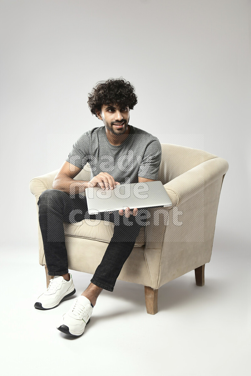 A man wearing casual sitting on a chair holding a laptop on white background