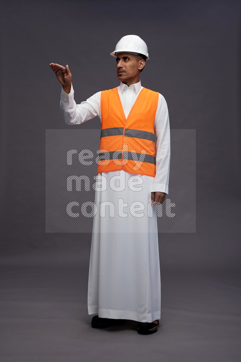 Saudi man wearing thob with engineer vest standing interacting with the camera on gray background