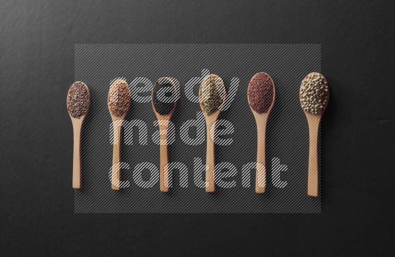 الفلفل الأسود وحبوب الخردل وحبة البركة وحب الرشاد والكمون و حبوب الكتان في معالق خشبية علي خلفية سوداء