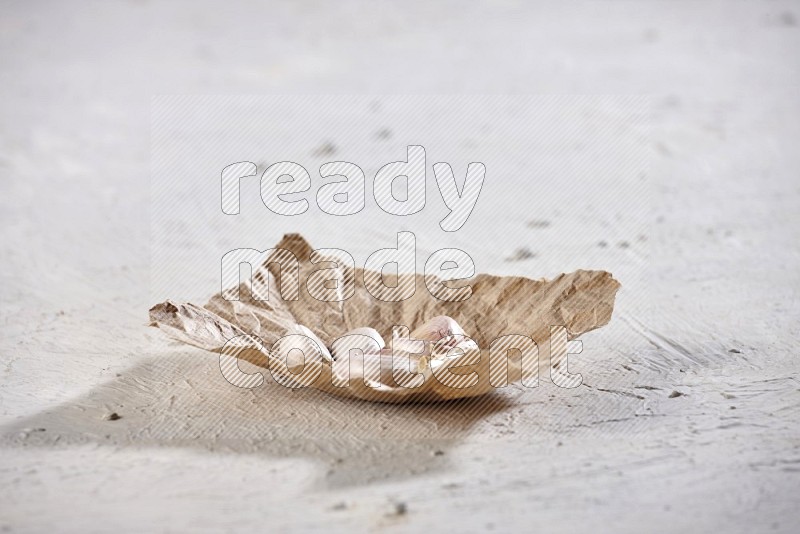 A crumpled piece of paper full of garlic cloves on a textured white flooring in different angles