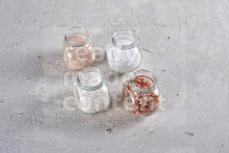 4 glass jars filled with table salt, coarse sea salt, fine himalayan salt and coarse himalayan salt on white background