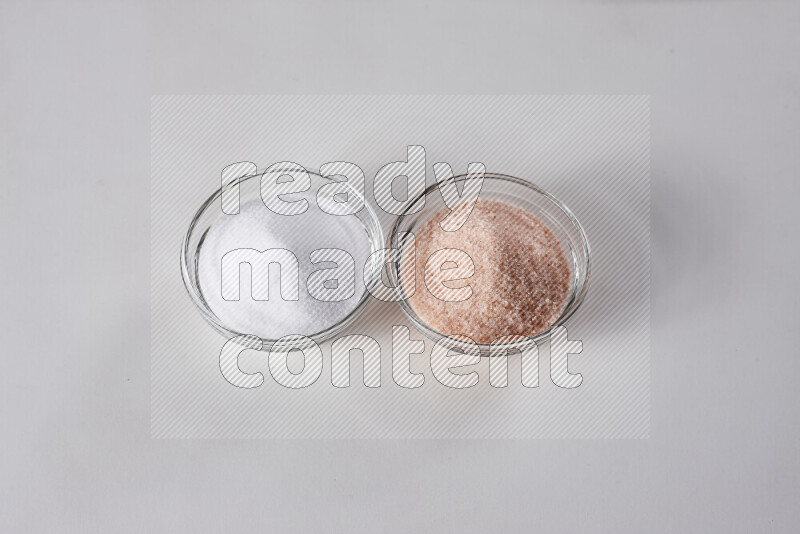 2 وعاء زجاجي احدهمها ممتلئ بملح الهيمالايا والأخر بالملح الأبيض على خلفية بيضاء