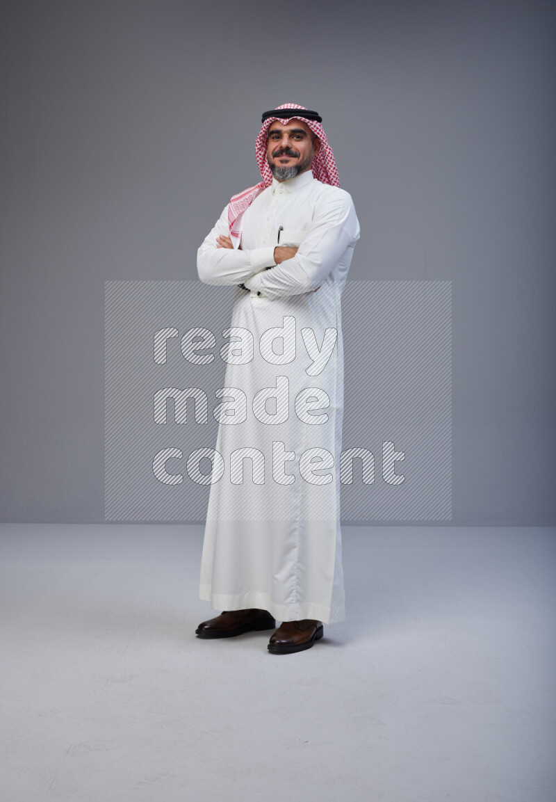Saudi man Wearing Thob and red Shomag standing with crossed arms on Gray background