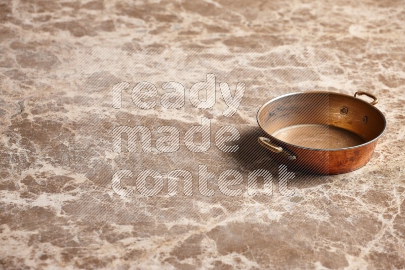A small copper pan on beige marble background