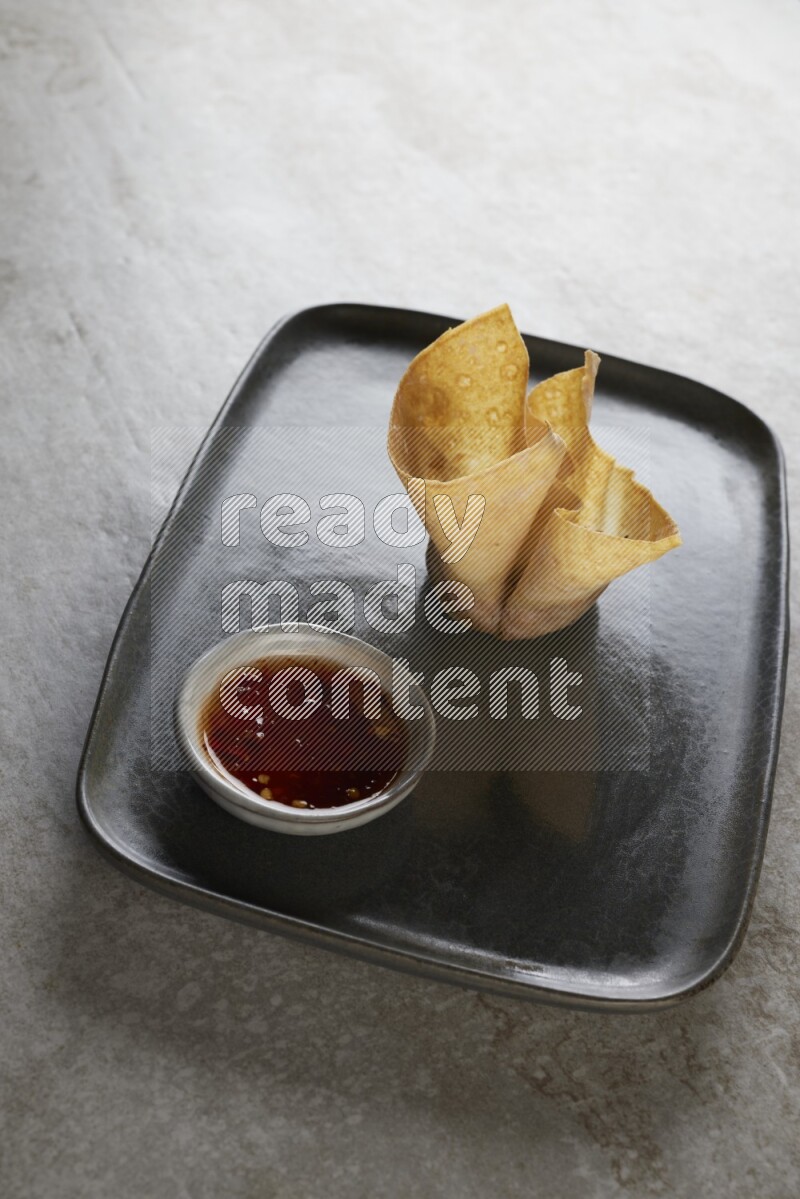 wonton cups with soy sauce ramkin on rectangle dark grey ceramic plate on grey textured counter top