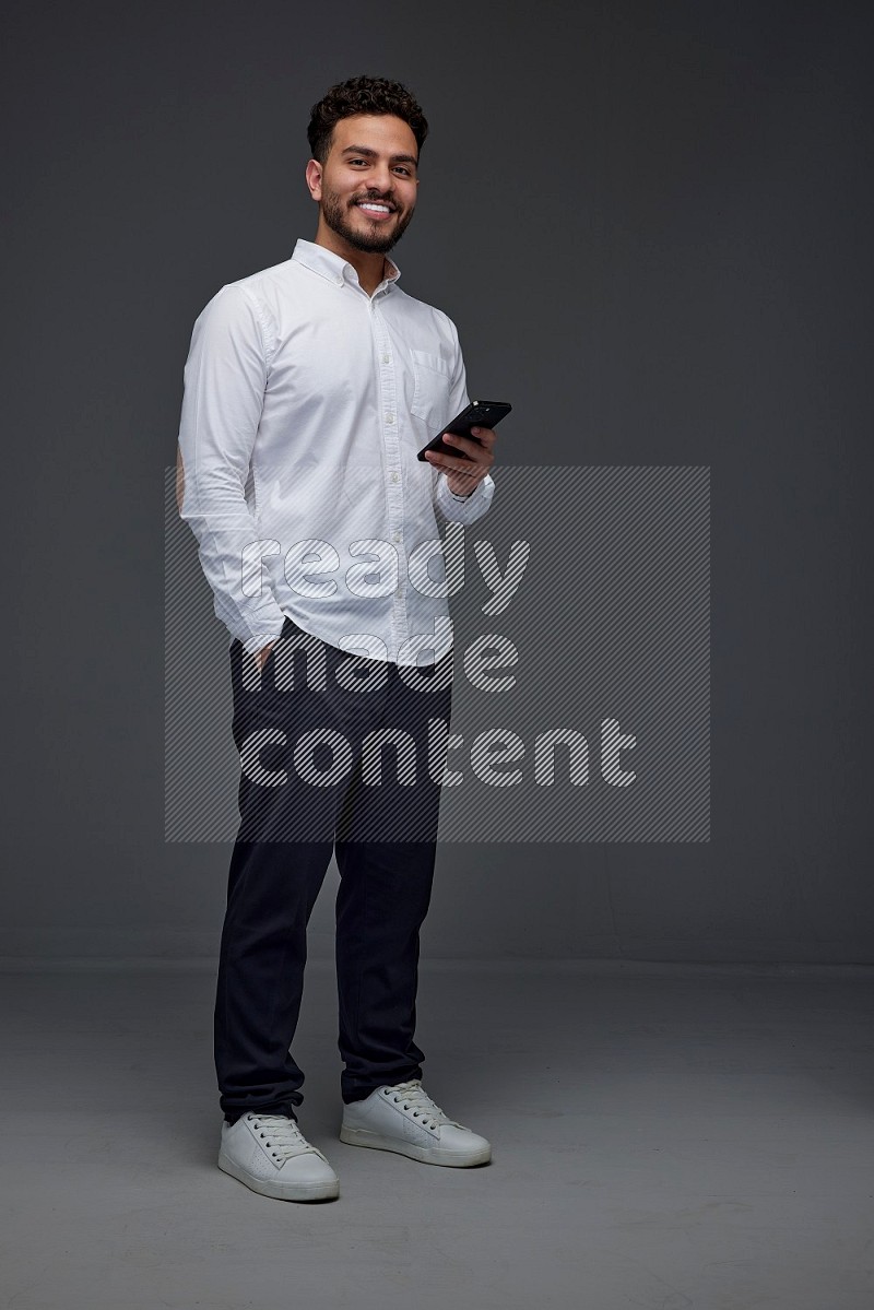 A man wearing smart casual standing and using his phone eye level on a gray background