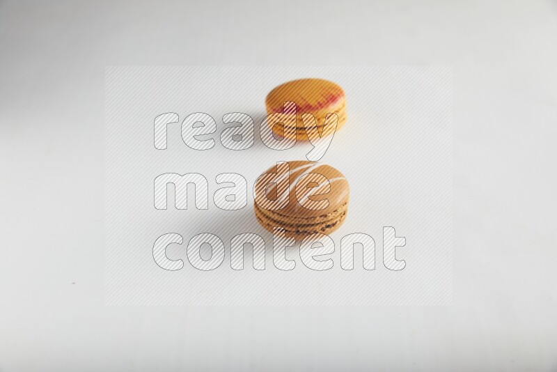 45º Shot of of two assorted Brown Irish Cream, and Orange Exotic macarons on white background