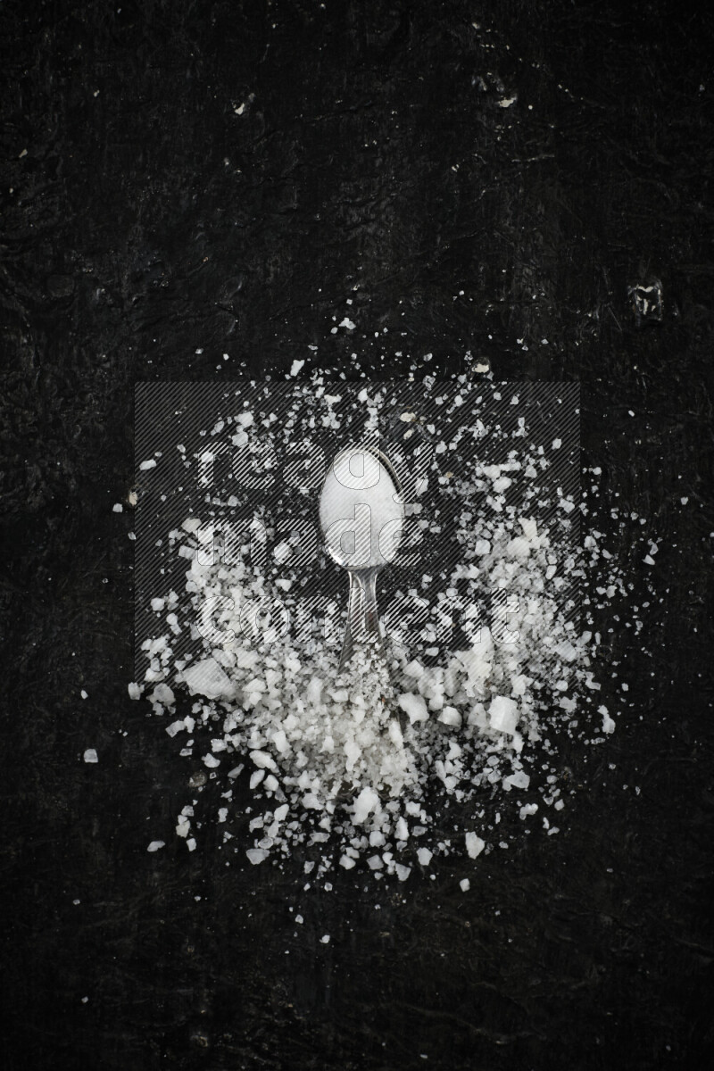 ملعقتان معدنيتان ممتلئتان بالملح الأبيض على خلفية سوداء