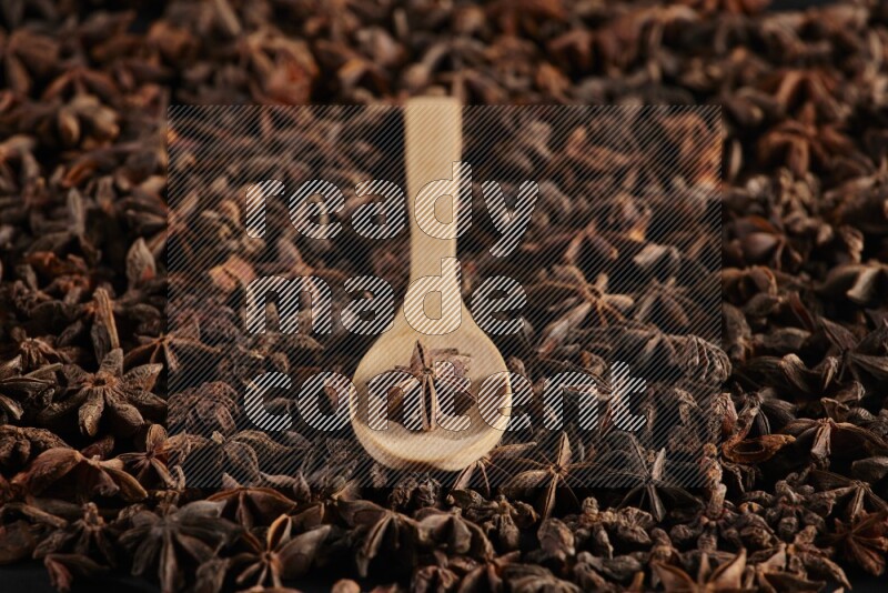 Star Anise in a wooden spoon on more stars anise filling the frame on black flooring