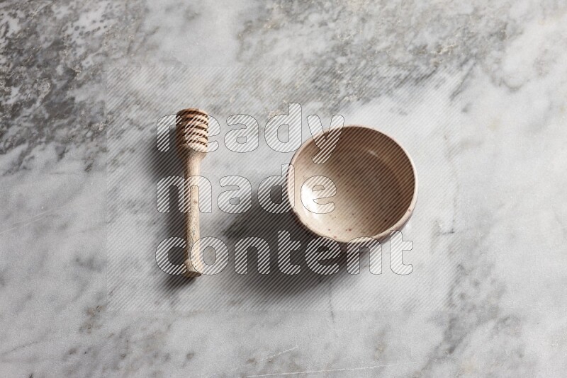 Beige pottery bowl with wooden honey dipper on the side on grey marble background
