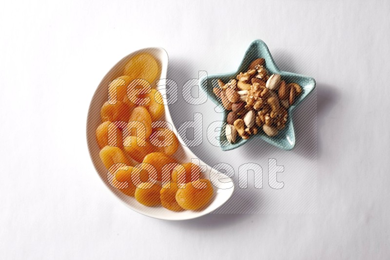 Dried apricots in a crescent pottery plate and a star shaped plate with mixed nuts on white background