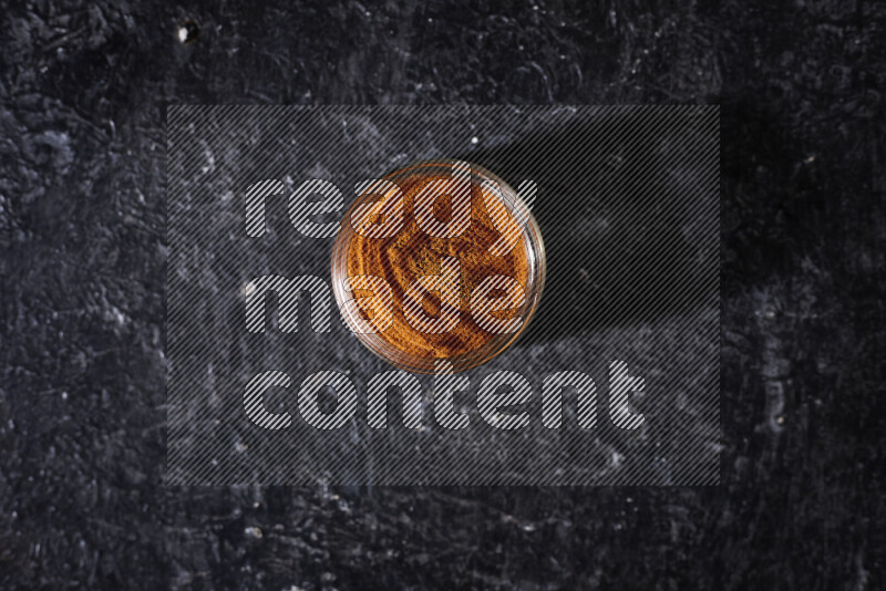 A glass jar full of ground paprika powder on black background