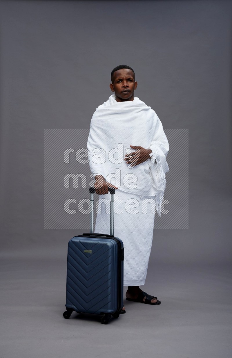 A man wearing Ehram Standing holding traveling bag on gray background