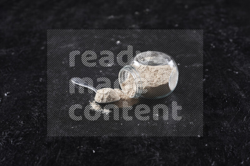 A glass jar full of onion powder flipped with some spilling powder on black background