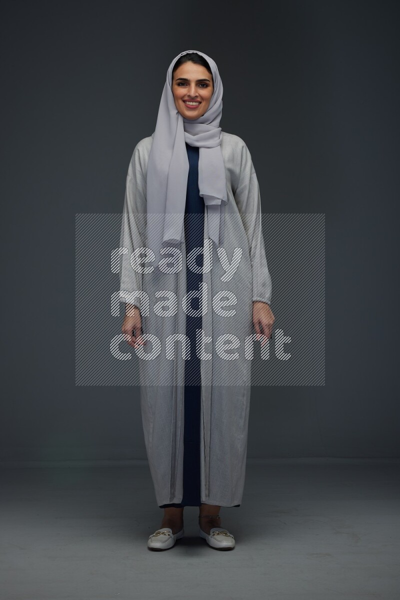 A Saudi woman wearing a light gray Abaya and head scarf standing and making multi poses eye level on a grey background