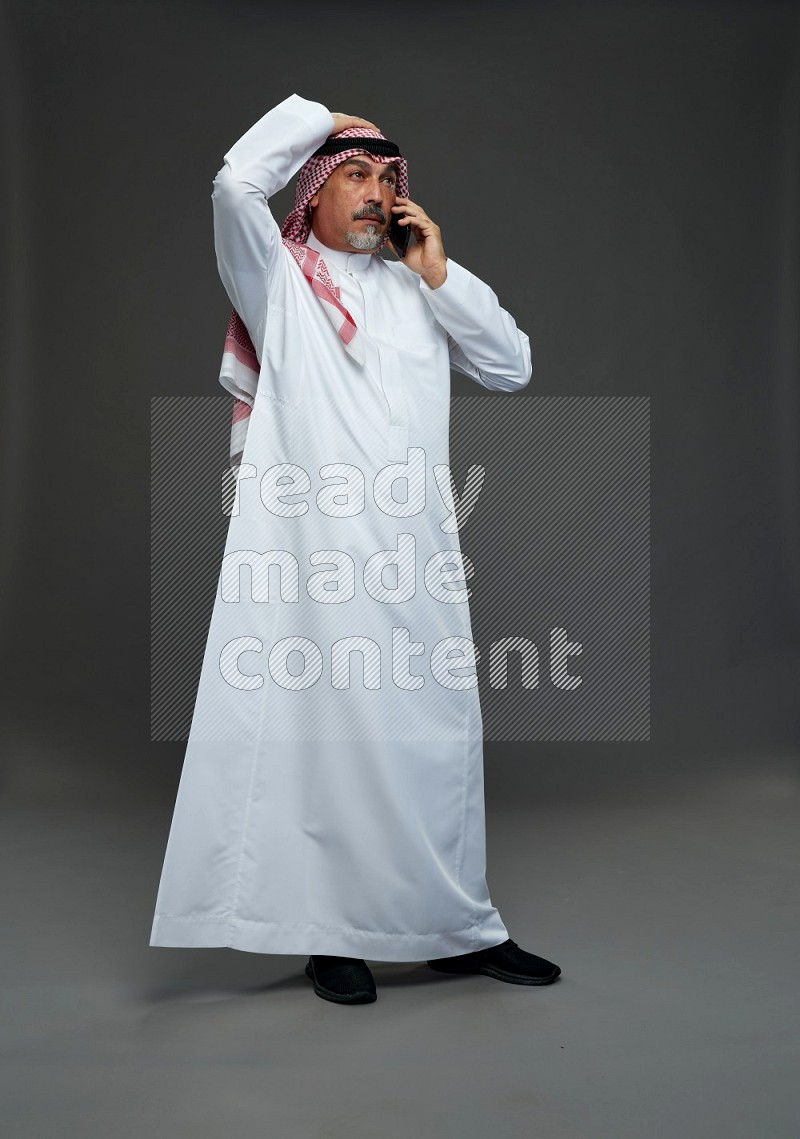 Saudi man with shomag Standing talking on phone on gray background