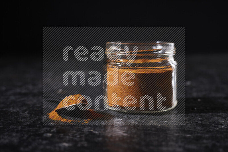 A glass jar full of ground paprika powder on black background