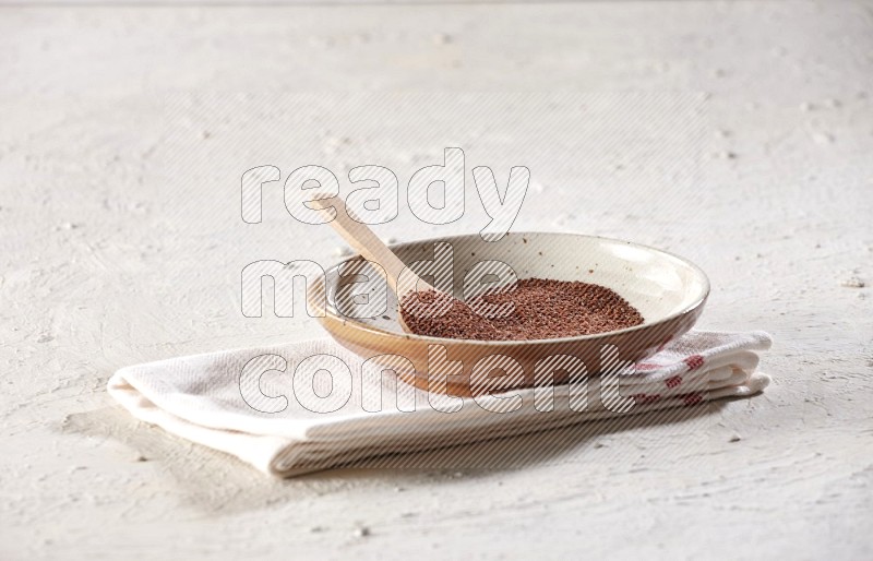 A multicolored pottery plate full of garden cress with a wooden spoon full of the seeds on a napkin on a textured white flooring in different angles
