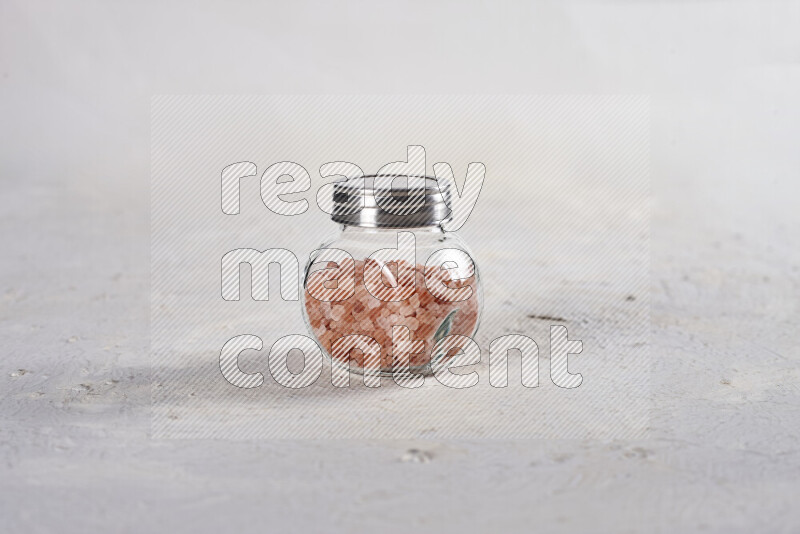 A glass jar full of coarse himalayan salt crystals on white background