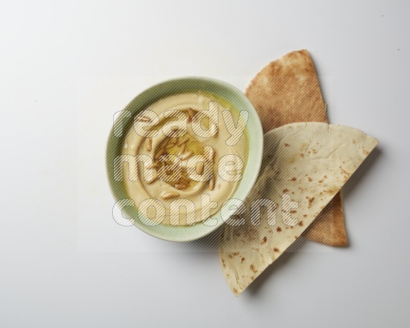 Hummus in a green plate garnished with pine nuts on a white background