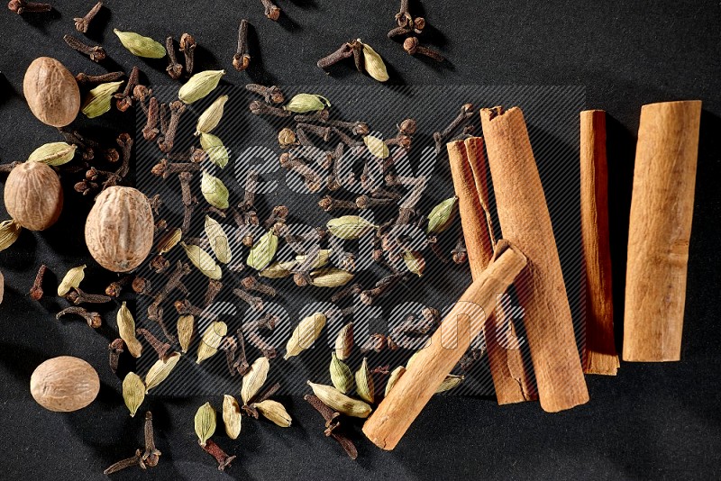 Cardamom, cloves, nutmeg and cinnamon sticks on black flooring