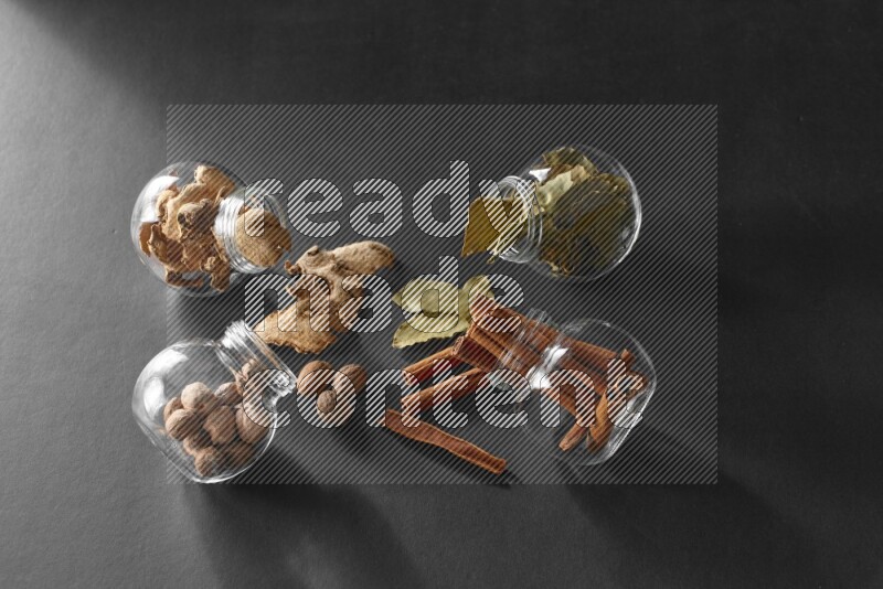 أوراق الغار وزنجبيل مجفف وقرفة وجوزة الطيب في أوعية زجاجية علي خلفية سوداء