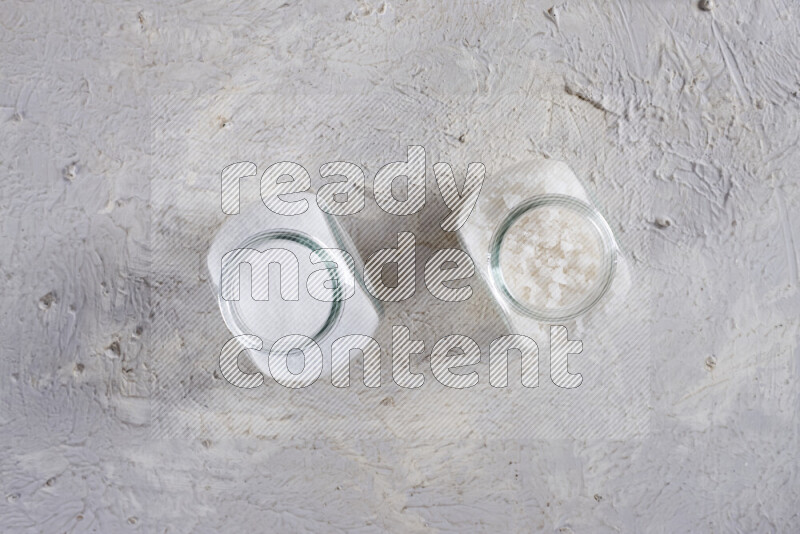 2 glass jars one is filled with table salt and the other with coarse sea salt on white background