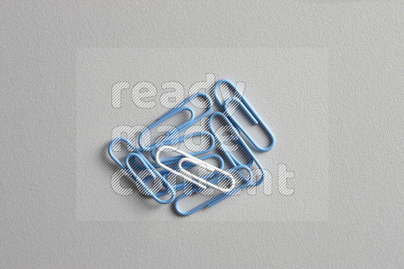 A white paperclip surrounded by bunch of blue paperclips on grey background