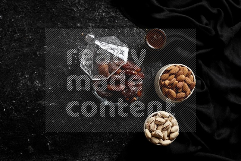 Dates in glass bowl with coffee and nuts in a dark setup