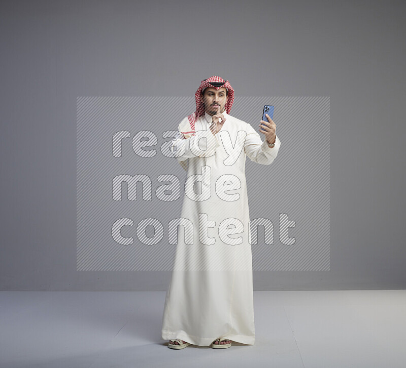 رجل سعودي يرتدي ثوب ابيض وشماغ احمر يقوم بمحادثه فيديو باستخدام جواله