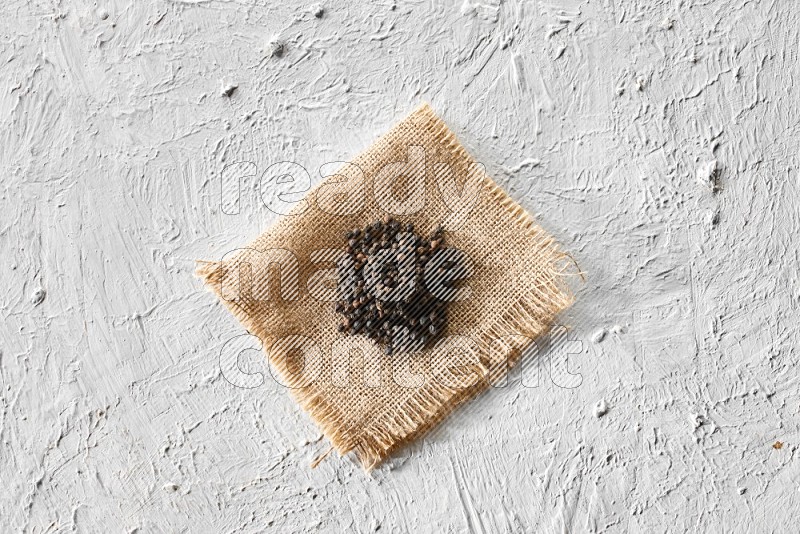 Black pepper on burlap fabric on a textured white flooring