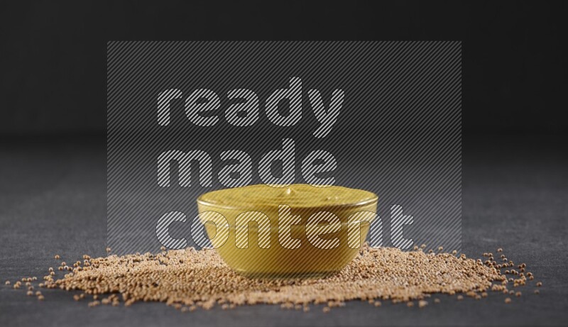 وعاء زجاجي مملوء بمعجون الخردل مع بذور الخردل تحته على أرضية سوداء