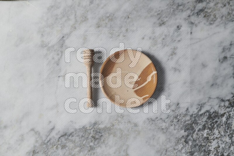 Multicolored pottery plate with wooden honey dipper on the side on grey marble background