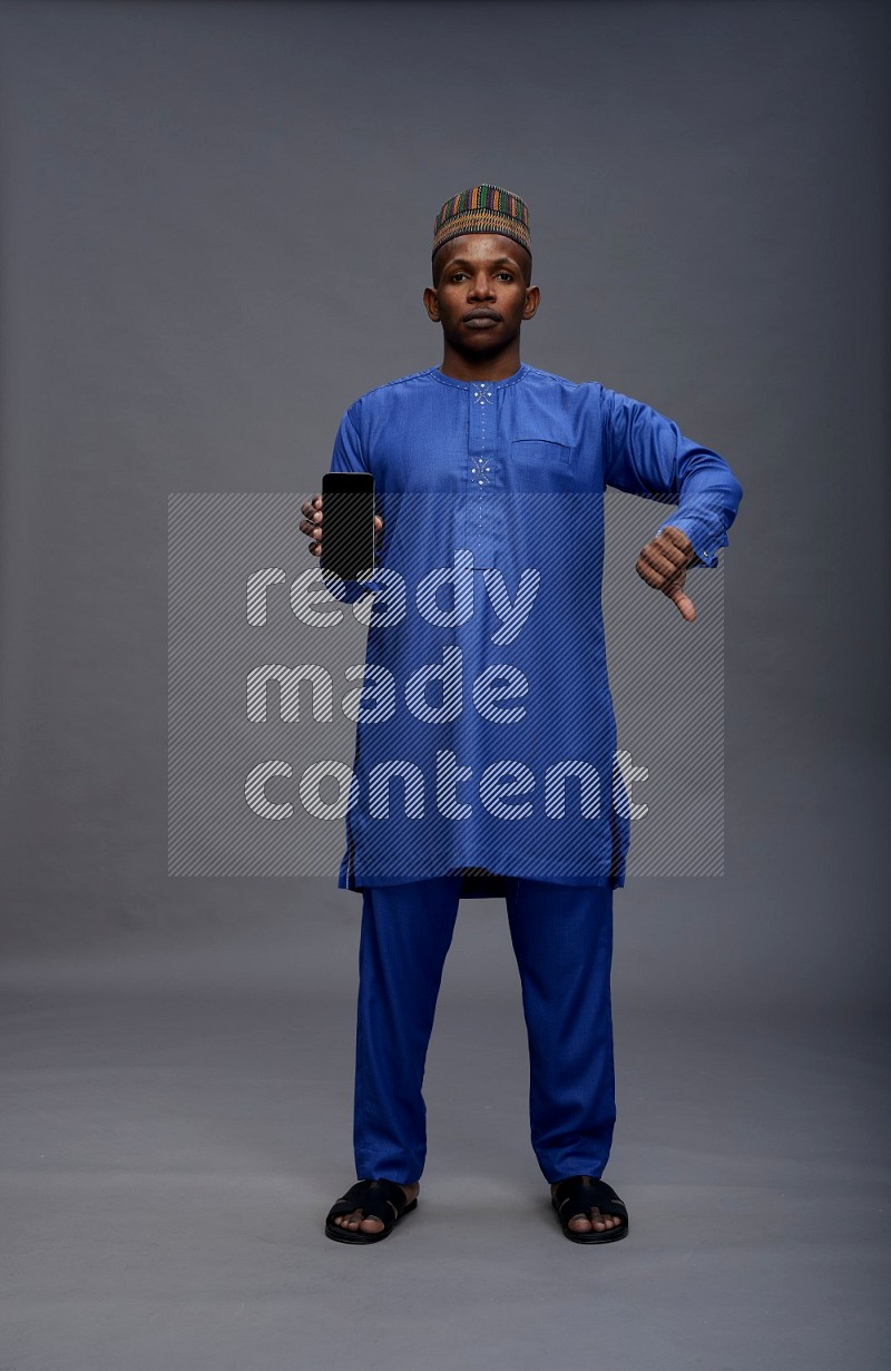 Man wearing Nigerian outfit standing showing phone to camera on gray background