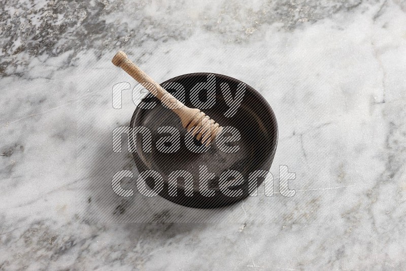Black Pottery Oven Plate with wooden honey handle in it, on grey marble flooring, 65 degree angle